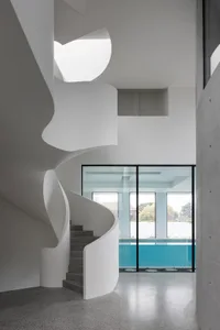 A minimalist house featuring a concrete spiral staircase leading to a pool area.