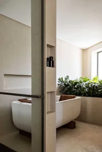Modern minimalist bathroom with concrete walls, a freestanding bathtub, and tropical plants.