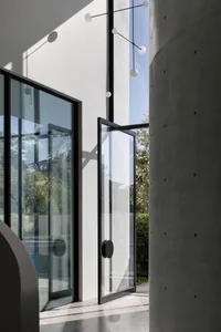 Modern entrance featuring transparent glass walls, sleek concrete columns, and black structural elements.