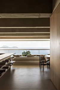 A modern home interior featuring concrete walls and wooden furniture with a view of the sea.