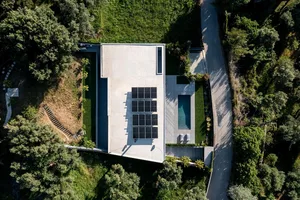 An aerial view of a modern house with concrete walls, a rooftop pool, and surrounding greenery.