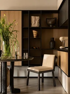 Modern kitchen with sleek wooden cabinets and metal accents, featuring a dining table and a tall vase with greenery.