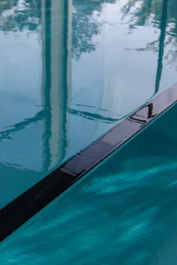 A sleek glass edge of a modern swimming pool reflecting the surroundings.