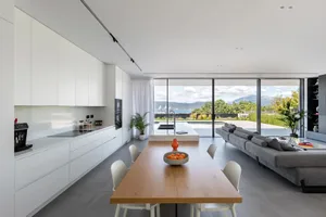 Contemporary kitchen with white cabinets and dark wood dining table, overlooking scenic outdoor view.