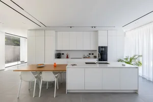 A modern kitchen with white concrete walls and white cabinets, featuring a large island with a wooden countertop.