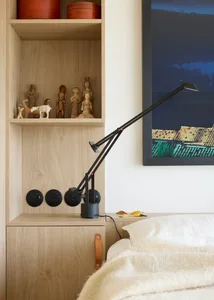 A minimalist bedroom with a modern desk lamp and wooden shelves.