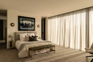 A minimalistic bedroom with a large bed, textured cotton bedding, and sheer curtains allowing natural light to enter.