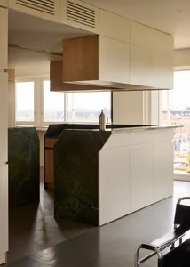 Modern minimalist kitchen featuring white cabinets, a marble island, and a concrete pendant light.