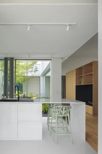 Modern minimalist kitchen with white cabinetry and open layout, featuring green bar stools and a large window overlooking a g
