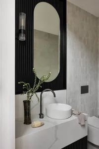A modern bathroom featuring a marble sink with a round basin and a sleek faucet. Decorative elements include a vase with gree