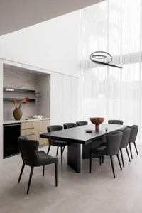 A modern dining room featuring a black wooden table surrounded by matching upholstered chairs, illuminated by a modern circul