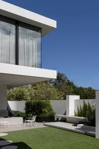 A modern house with large glass windows, concrete elements, and greenery in the garden.