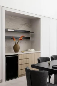 A modern kitchen interior featuring wooden cabinets, marble countertops, and a wine fridge.