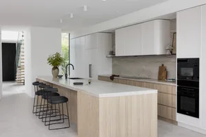 Modern kitchen with white cabinets, marble countertops, black stools, and light wood elements.