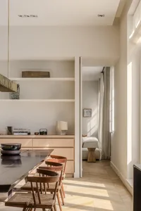 Modern minimalist dining room featuring a wooden table, chairs, and shelving unit with books and decorative items.
