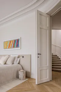 Minimalist residential interior with a bed, colorful abstract painting, and a staircase.
