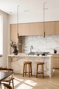Modern minimalist residential kitchen with a white marble countertop and wooden stools.