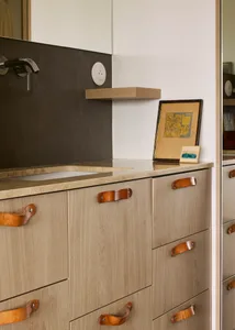 A modern bathroom cabinet featuring a wooden structure with leather handles and a beige marble countertop.