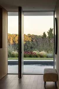Modern exterior with large glass doors, pool, and lush garden view at dusk.
