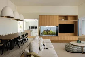 A modern living room featuring a beige sofa, a wooden entertainment center with a large flat-screen TV, and a dining area wit