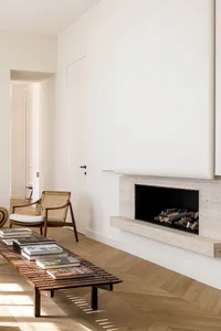 A minimalist living room with a modern stone fireplace and books arranged on a bench.