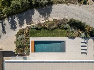 Aerial view of a modern residential pool with concrete patio and surrounding garden.