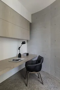 A modern, sleek workstation with a wooden desk and black lamp positioned against a concrete wall.