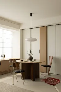 A minimalist dining room with a round wooden table, chairs, and a pendant light.