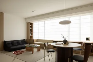 Modern minimalist living space with a black sofa, round wooden table, and contemporary furniture.