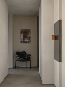 Modern interior design featuring a minimalist concrete wall with a sleek black armchair and a contemporary art piece.