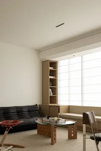 A modern living room with minimalist design, featuring a black leather sofa, a wooden coffee table, and a large window with a