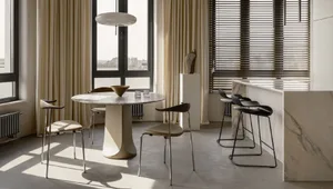 A modern kitchen with marble countertops and floor, featuring wooden chairs and a large round table.