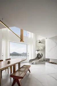 Modern living room featuring a circular white marble and stainless steel slide, with large windows overlooking a scenic view.