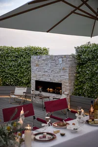 Evening scene of an outdoor dining area with stone brick fireplace, white lighting, and table setting.
