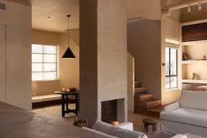A minimalist living room featuring exposed brick walls, wood furniture, and a brick fireplace.