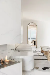 Modern minimalist living room featuring marble fireplace and furniture, with a view of a cityscape through an archway.