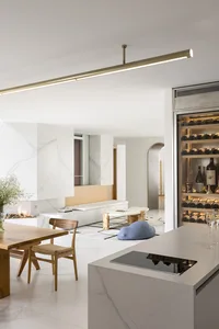 A modern kitchen with white marble countertops, wooden furniture, and a fireplace.