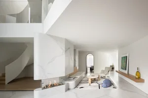 Modern minimalist living room with marble walls and floor, white furniture, and a spiral staircase.