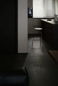 A minimalist kitchen with dark wood flooring, black stools, and sleek, modern appliances.