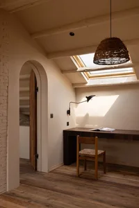 A minimalist home office with a timber floor, featuring a wooden desk, chair, and wicker pendant light under a skylight.