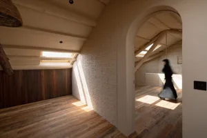 Modern minimalist room with wooden floors, brick walls, and sunlight filtering through an arched ceiling with skylights.