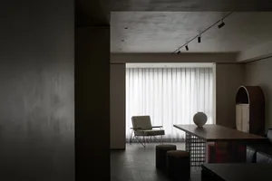 A minimalist living room featuring neutral-toned decor and a large window allowing natural light to enter.