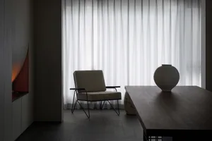 An elegant, minimalist living room features textured cotton curtains, wooden furniture, and a comfortable armchair against a 