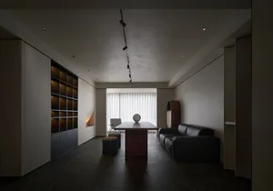 簡約客廳內擺放木質餐桌，桌上置有玻璃擺飾，搭配黑色皮革沙發與現代壁爐