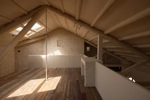 Modern minimalist attic space with exposed wooden beams, brick accents, and a skylight allowing natural light to enter.