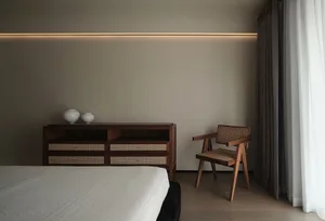 A minimalist white bedroom with textured wooden furniture and white curtains.