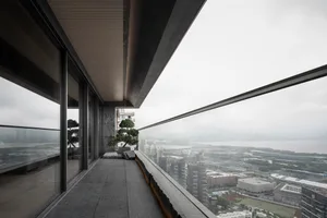 Modern balcony overlooking cityscape with a bonsai tree and outdoor seating.