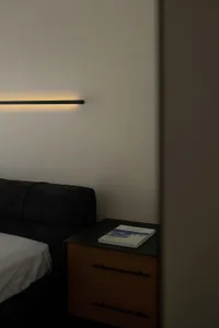 A modern bedroom featuring a wooden nightstand with a book on top, illuminated by a sleek linear light fixture mounted on the