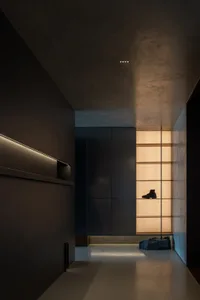 A minimalist modern entryway with a concrete floor, black cabinets, and warm lighting.