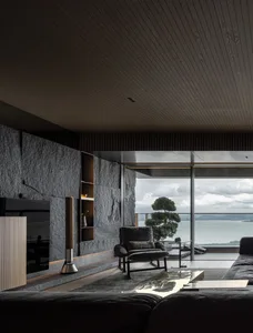 Modern minimalist living room with stone accent wall, concrete floor, and metal furniture.